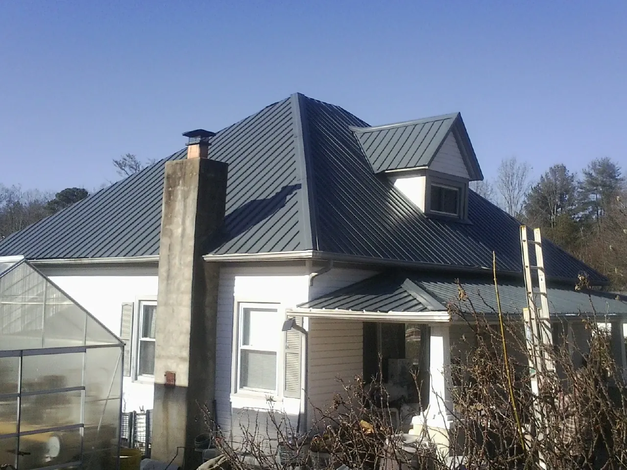 Dark blue standing seam metal roof on a white farmhouse with dormer — Slate & Tile Roof Repair by Roofing Brothers in Albert Lea