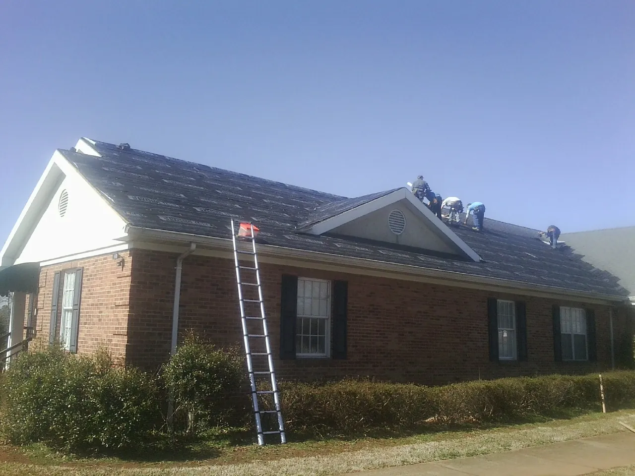 Crew tearing shingles off a brick ranch roof with a ladder set — Emergency Roof Repair work by our crew in Albert Lea