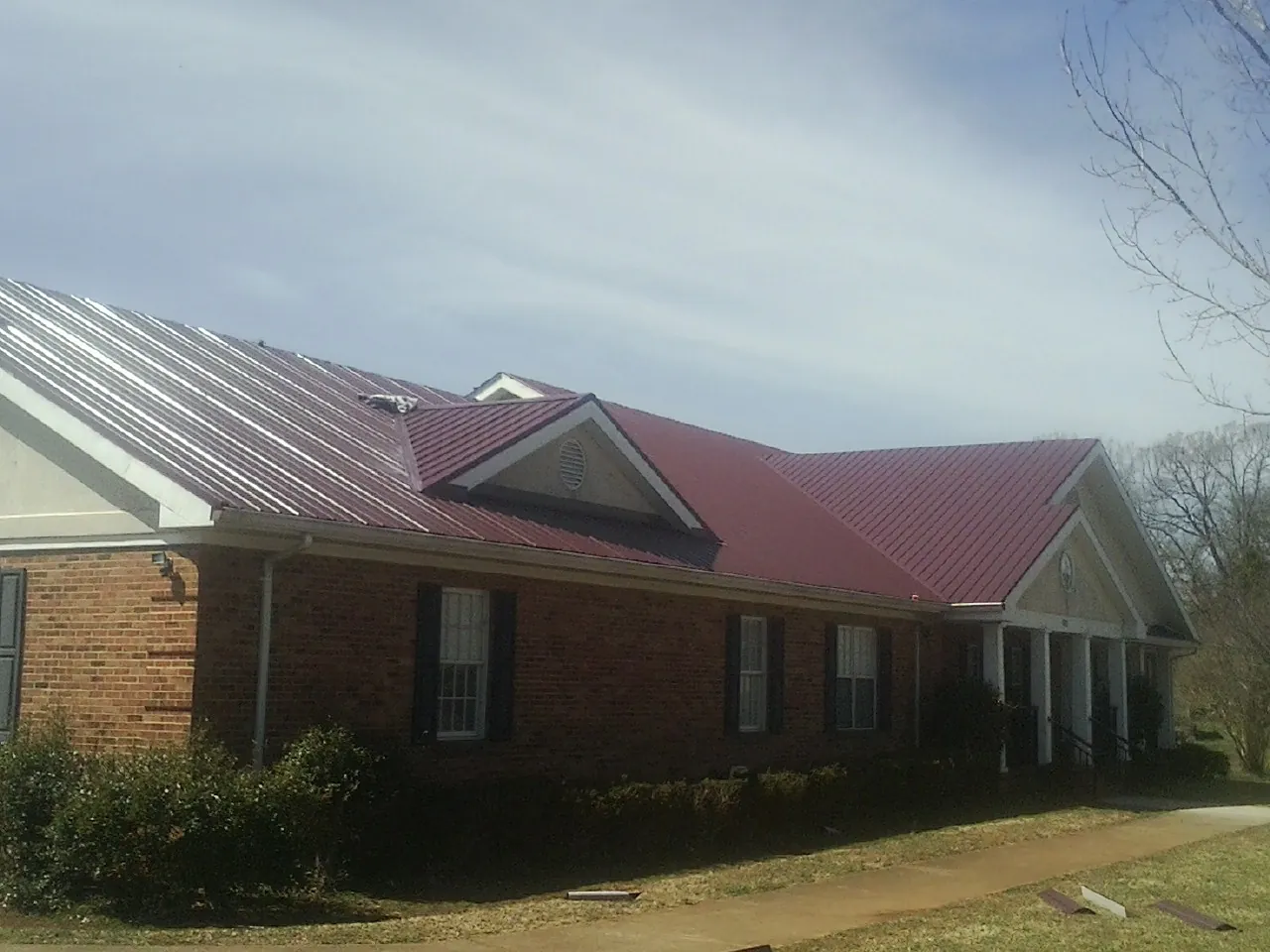 Red metal roof with gabled entries on a long brick building, from a Hail Damage Roof Repair job in Albert Lea