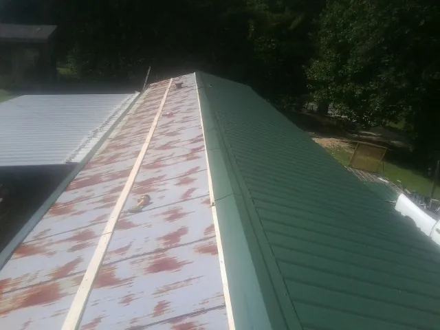 Old rusted panels beside newly installed green metal roofing — Wind Damage Roof Repair by Roofing Brothers in Albert Lea