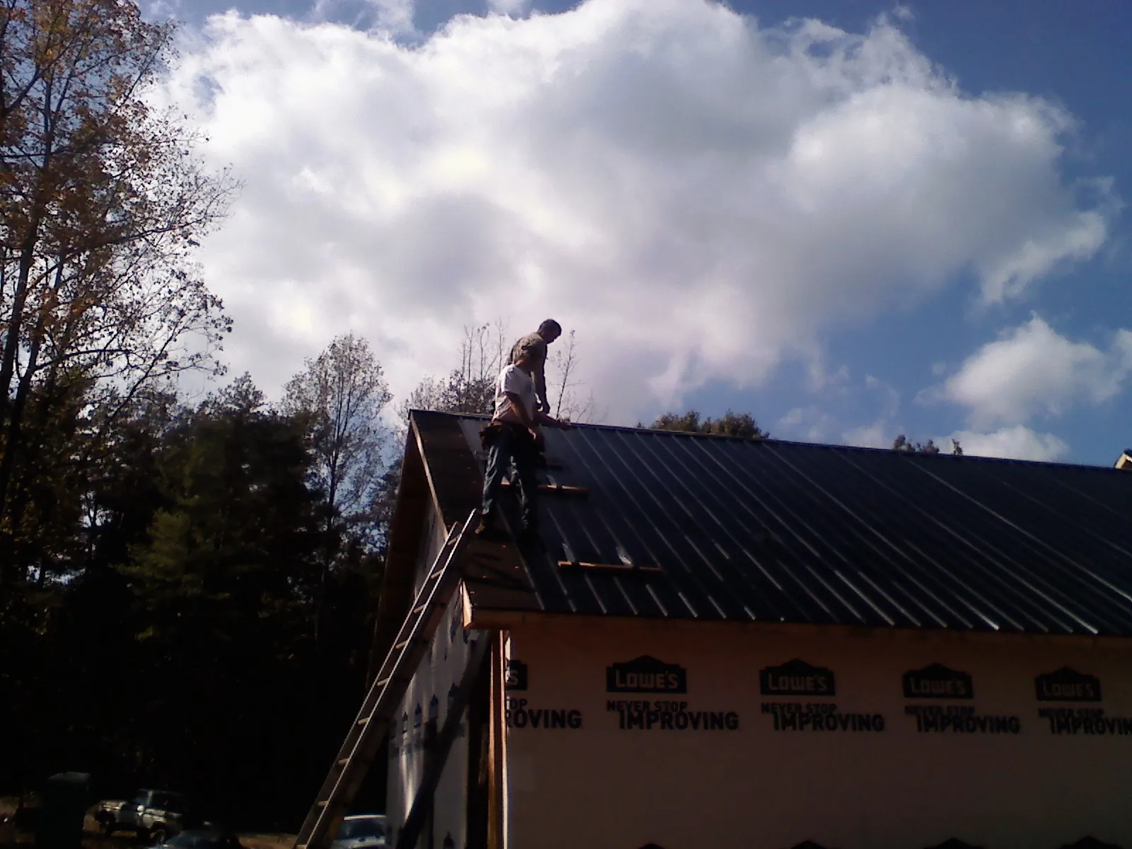 Roofer fastening dark metal panels high against a cloudy sky, from a Roof Inspection job in Albert Lea
