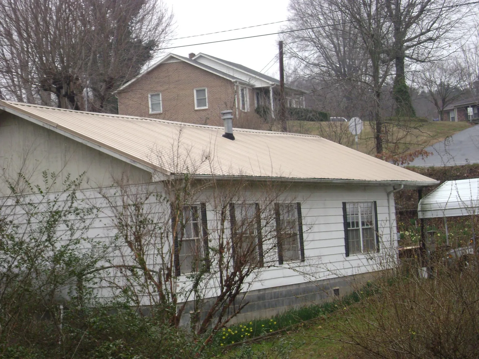 Tan metal roof on a white sided house set into a hillside — Commercial Roofing by Roofing Brothers in Albert Lea
