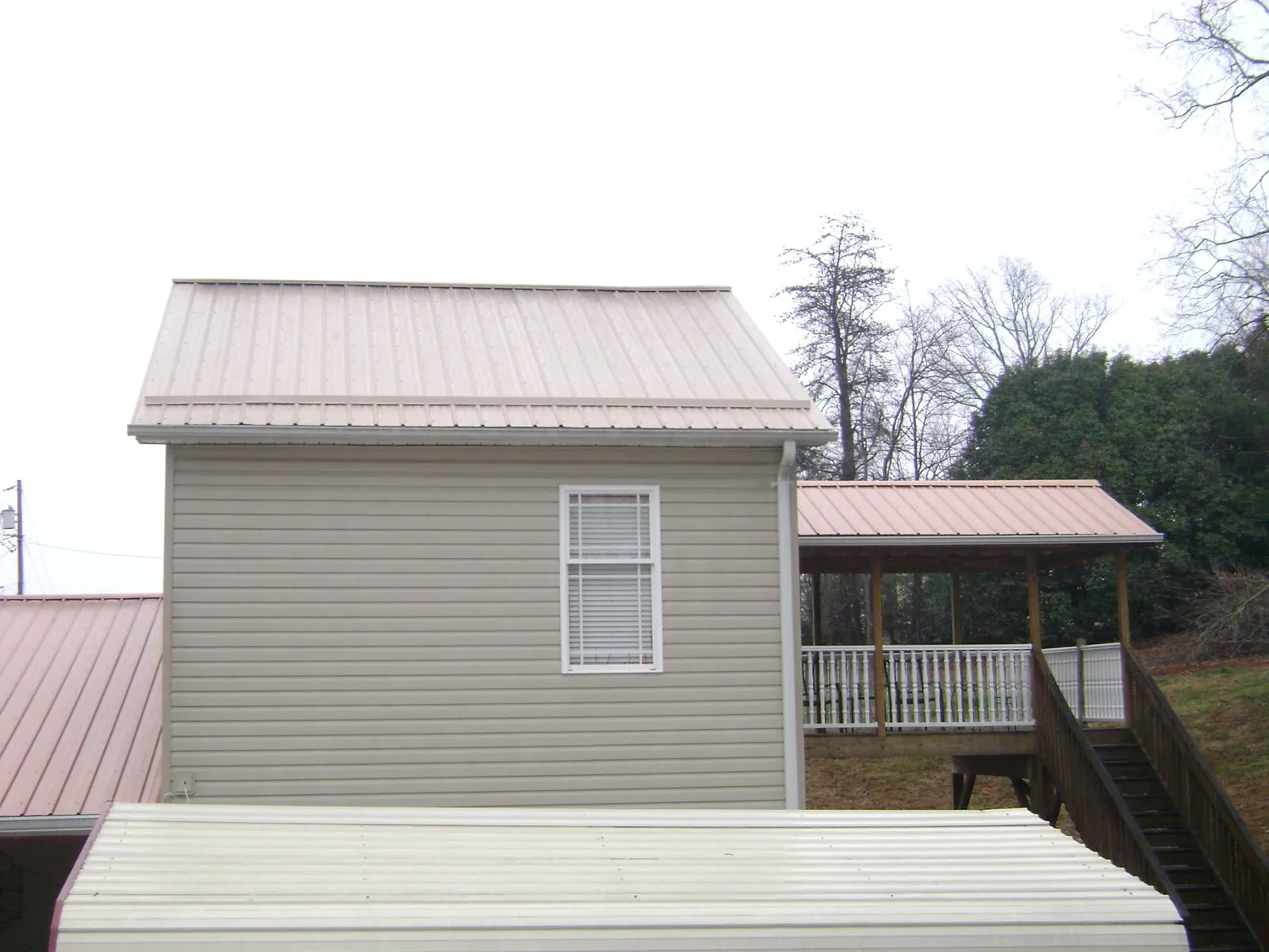 Tan metal roofs on a two story addition and attached porch, from a Roof Replacement job in Albert Lea